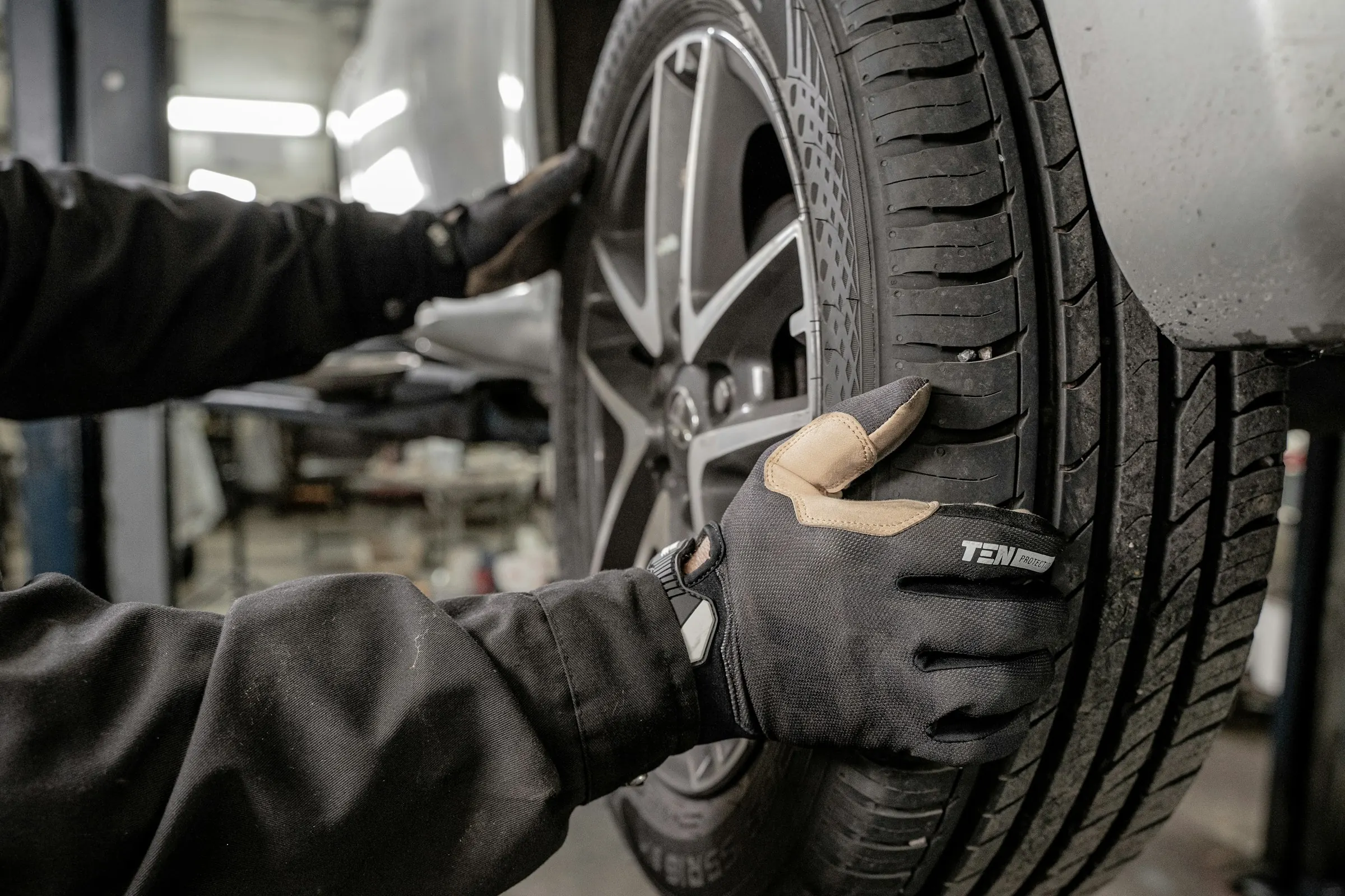 Mechanik w rękawicach zdejmuje koło z samochodu na podnośniku